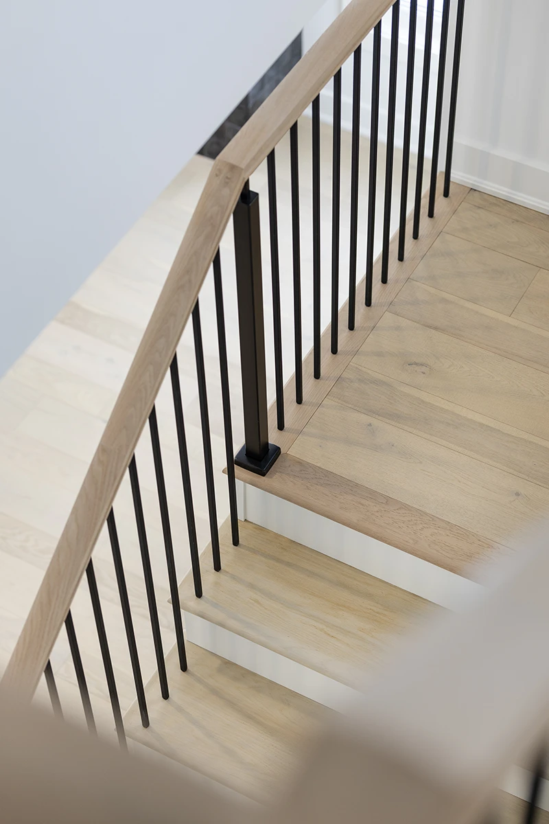Black metal balusters installed beneath a stained wood handrail.