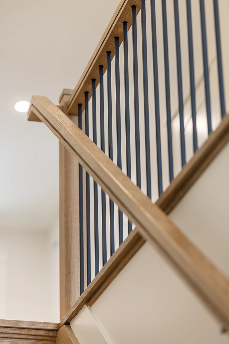 Corner detail of stained wood handrail and black metal balusters.