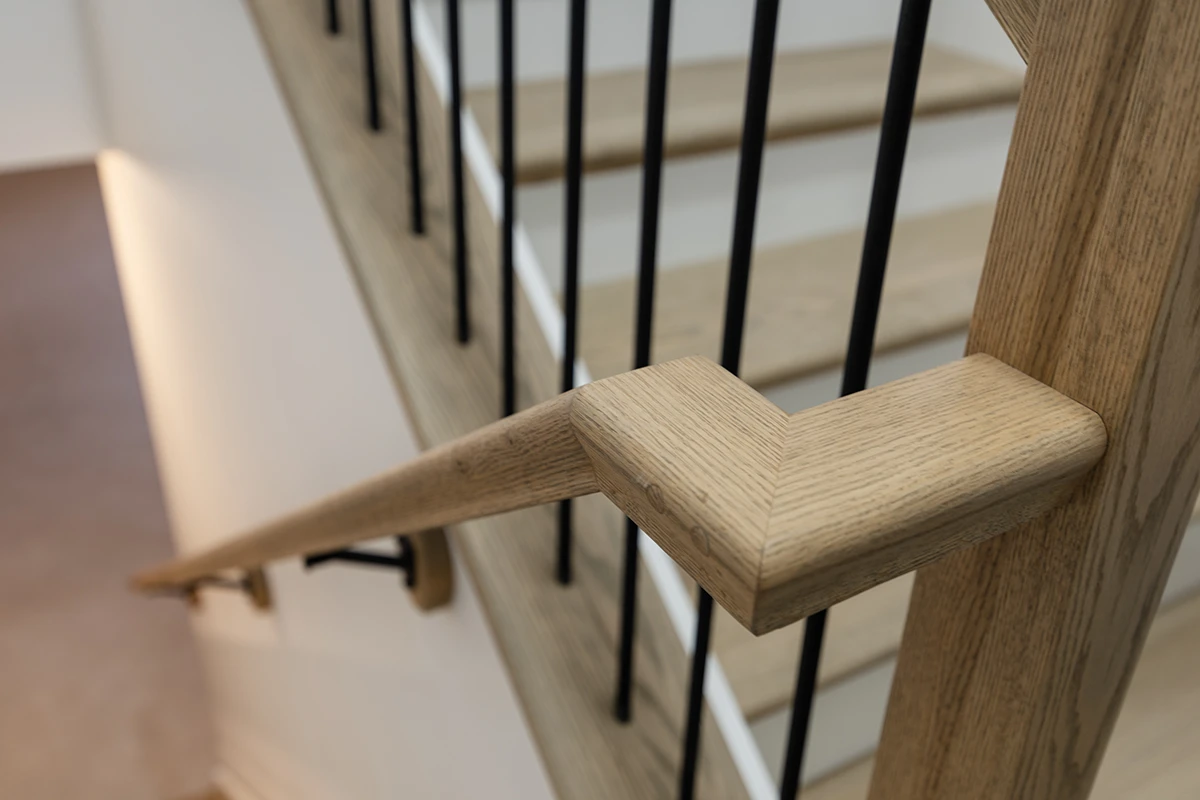 Close-up of stained wood stair tread with black metal balusters.