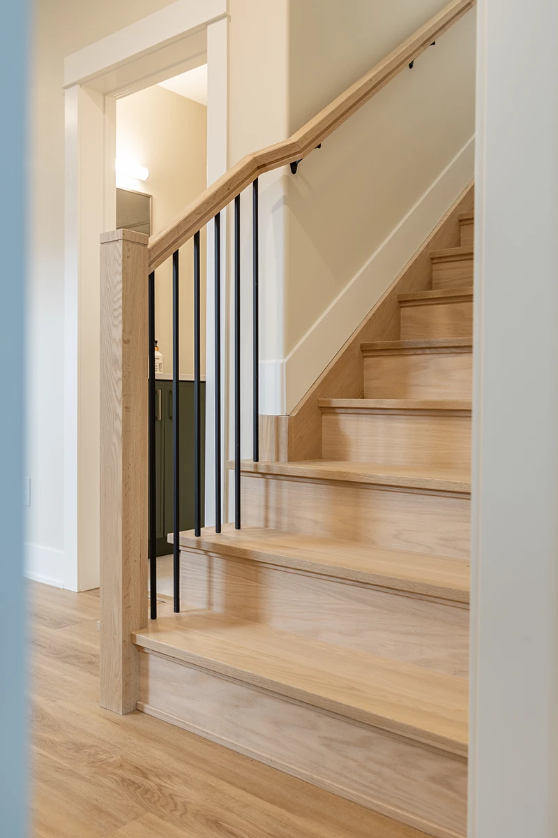 Staircase with black metal balusters and stained wood handrail.