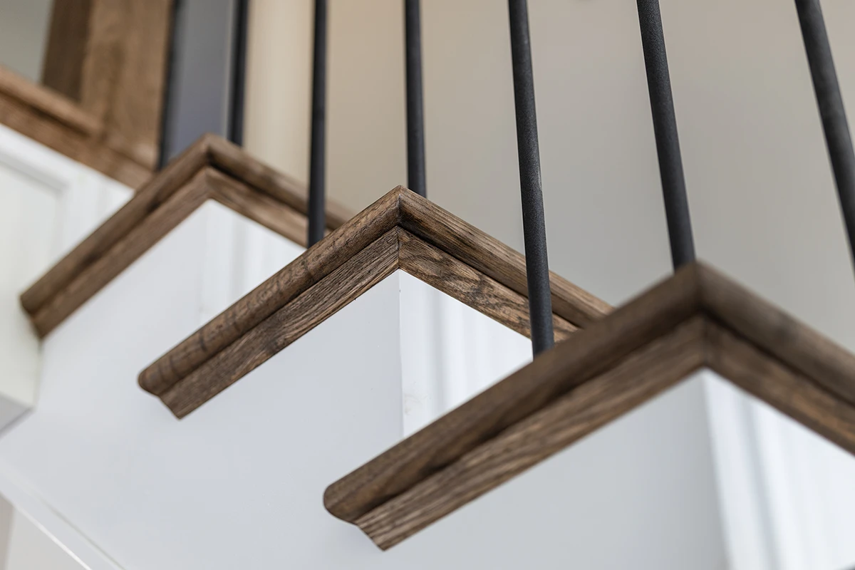 Corner detail of stained wood handrails with black metal balusters.