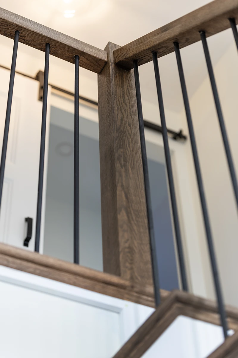 Square wood newel post with black metal balusters and wood handrail.