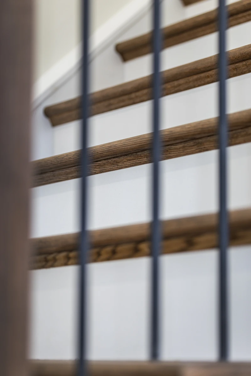 Close-up of stained wood stair treads with black metal balusters.