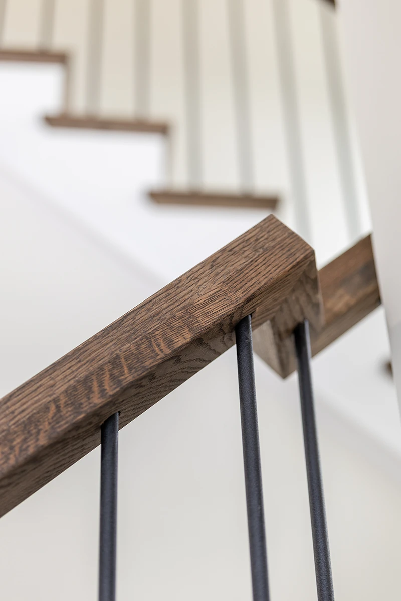 Detail of a stained wood handrail and black metal balusters.