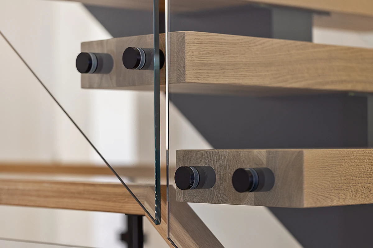 Black glass railing clamps mounted to oak stair treads.