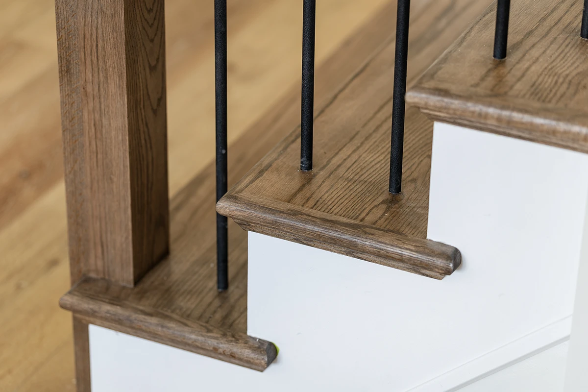 Close-up of oak stair tread with black metal balusters.