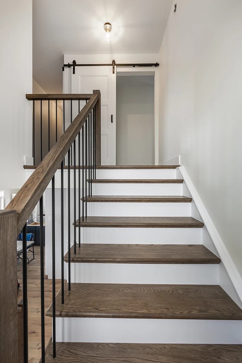 Straight wood staircase with black metal railings and white walls.